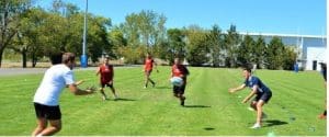 Plusieurs joueurs de rugby s'entraînent sur un terrain en herbe sous un ciel dégagé.